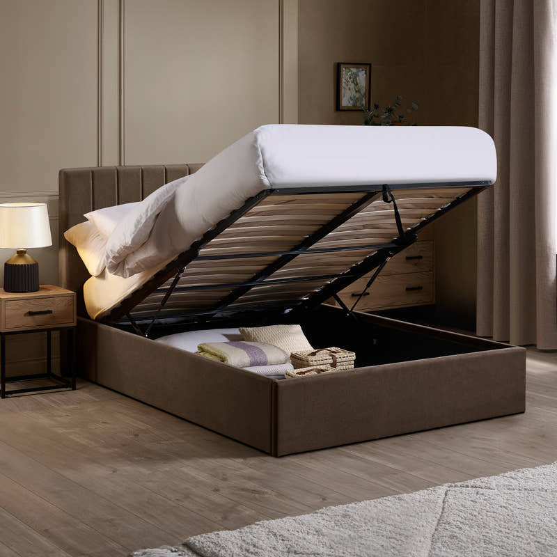 Aylen chocolate velvet ottoman bed with the base lifted to show the storage, in a bedroom