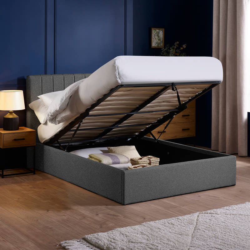 Aylen dark grey ottoman bed with the base lifted to show the storage, in a bedroom