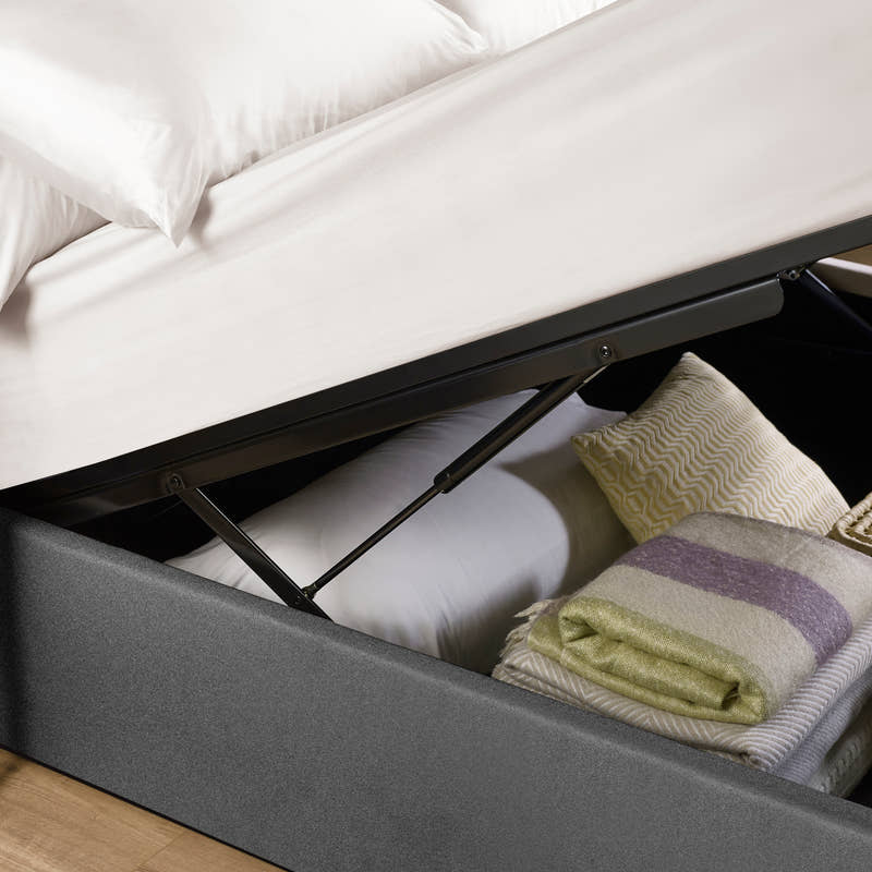 Aylen ottoman bed: gas lift raising the dark grey base over folded blankets, close up