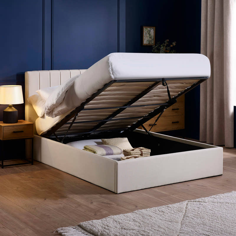 Aylen oatmeal ottoman bed with the base lifted to show the storage, in a bedroom