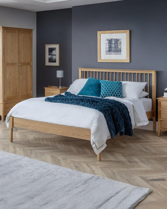 Julian Bowen Cotswold oak bed with a spindle headboard, in a bedroom with a dark blue wall