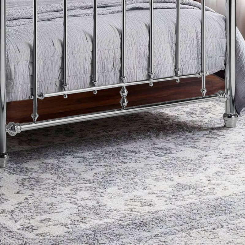Julian Bowen Empress chrome bed: lower footboard rail and feet on a grey rug, close up
