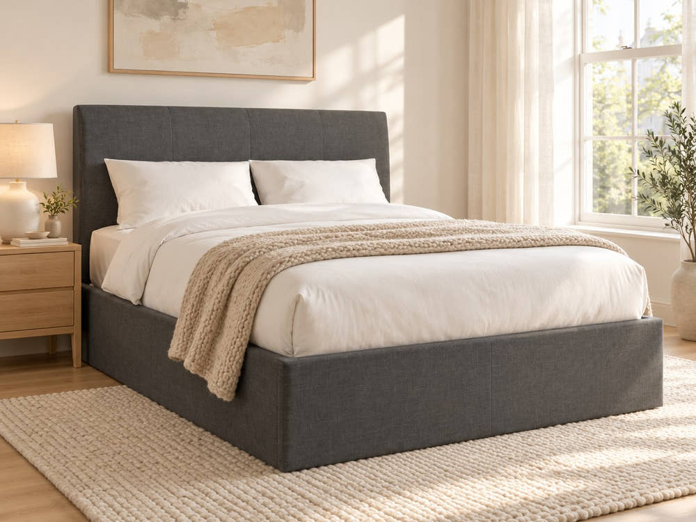 Sydenham grey fabric ottoman bed with a tall 115 cm headboard, in a bright bedroom (AI-generated illustration of this frame; bedding for illustration, mattress not included)
