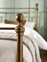 Aurelia bed: a round brass effect finial on the footboard, close up