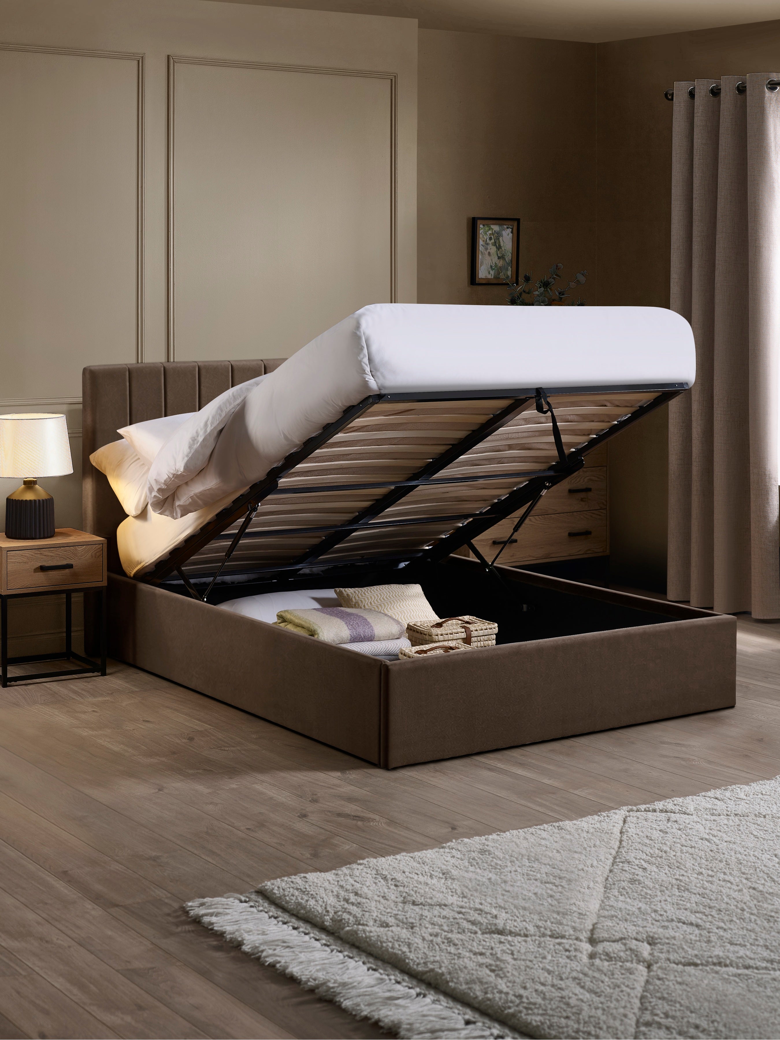 Aylen chocolate velvet ottoman bed with the base lifted to show the storage, in a bedroom