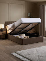 Aylen chocolate velvet ottoman bed with the base lifted to show the storage, in a bedroom