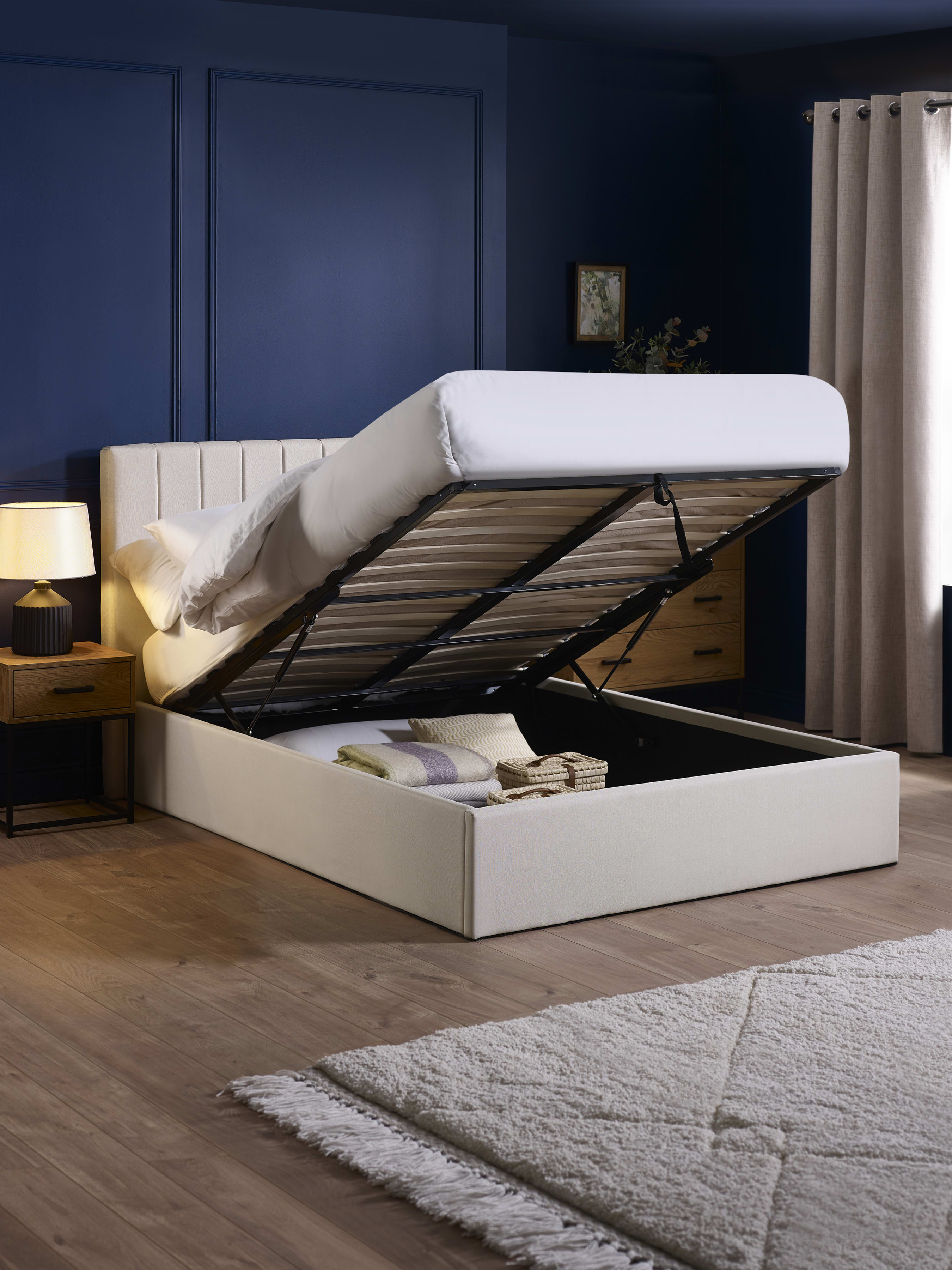 Aylen oatmeal ottoman bed with the base lifted to show the storage, in a bedroom