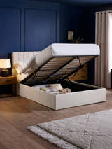 Aylen oatmeal ottoman bed with the base lifted to show the storage, in a bedroom