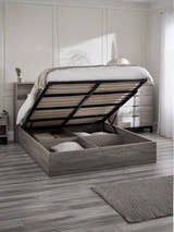 Bali grey oak effect ottoman bed with the gas lift base raised over the storage, in a bedroom