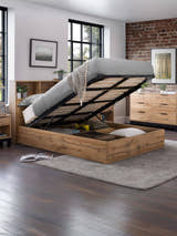 Bali light oak effect ottoman bed with the base raised over the storage, in a bedroom