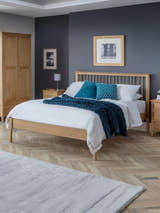 Julian Bowen Cotswold oak bed with a spindle headboard, in a bedroom with a dark blue wall
