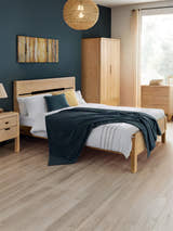 Julian Bowen Curve oak bed with a cut-out headboard, in a bedroom with a dark blue wall