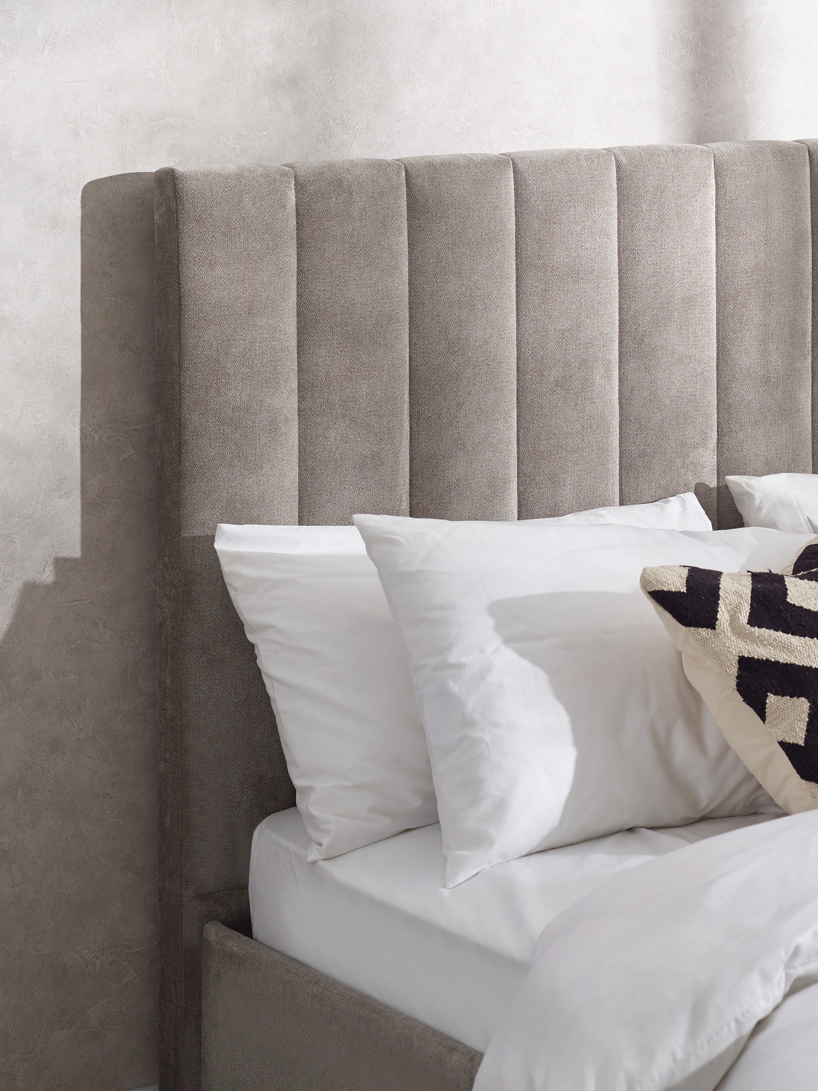 Eloise bed: tall grey chenille headboard behind white pillows, close up