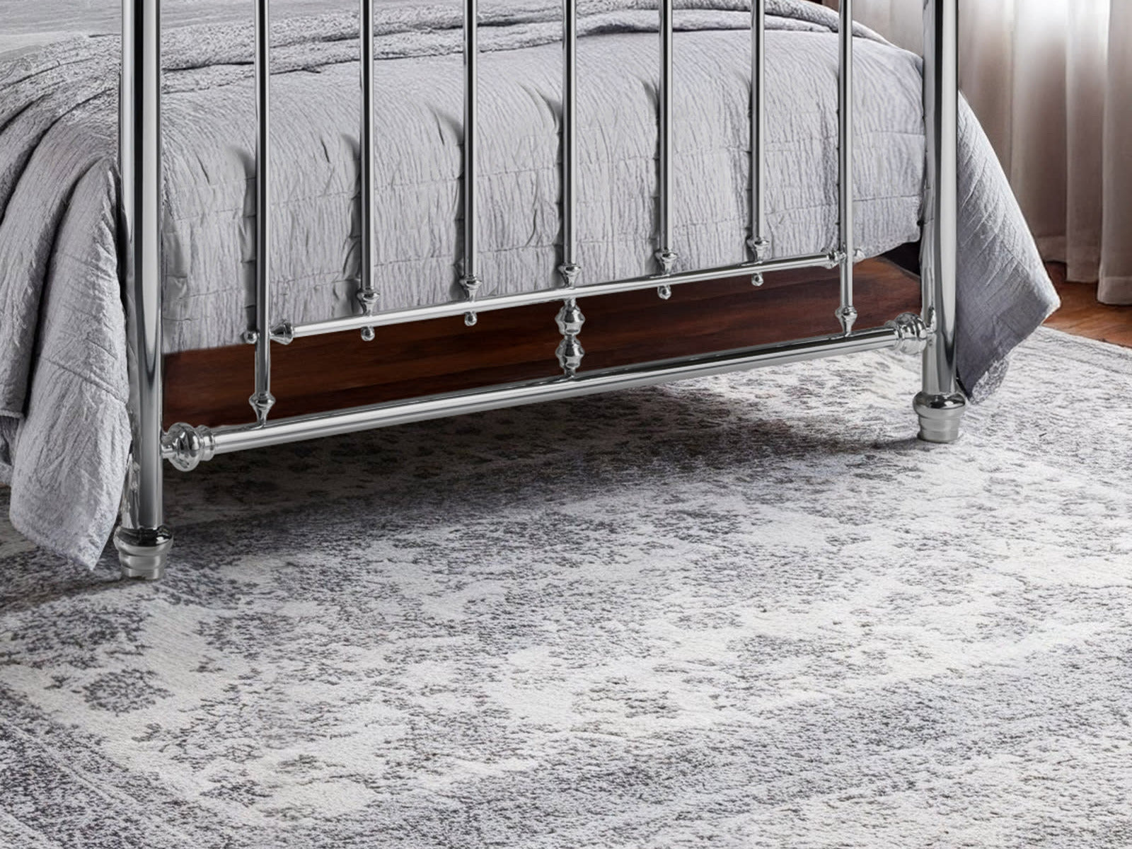 Julian Bowen Empress chrome bed: lower footboard rail and feet on a grey rug, close up