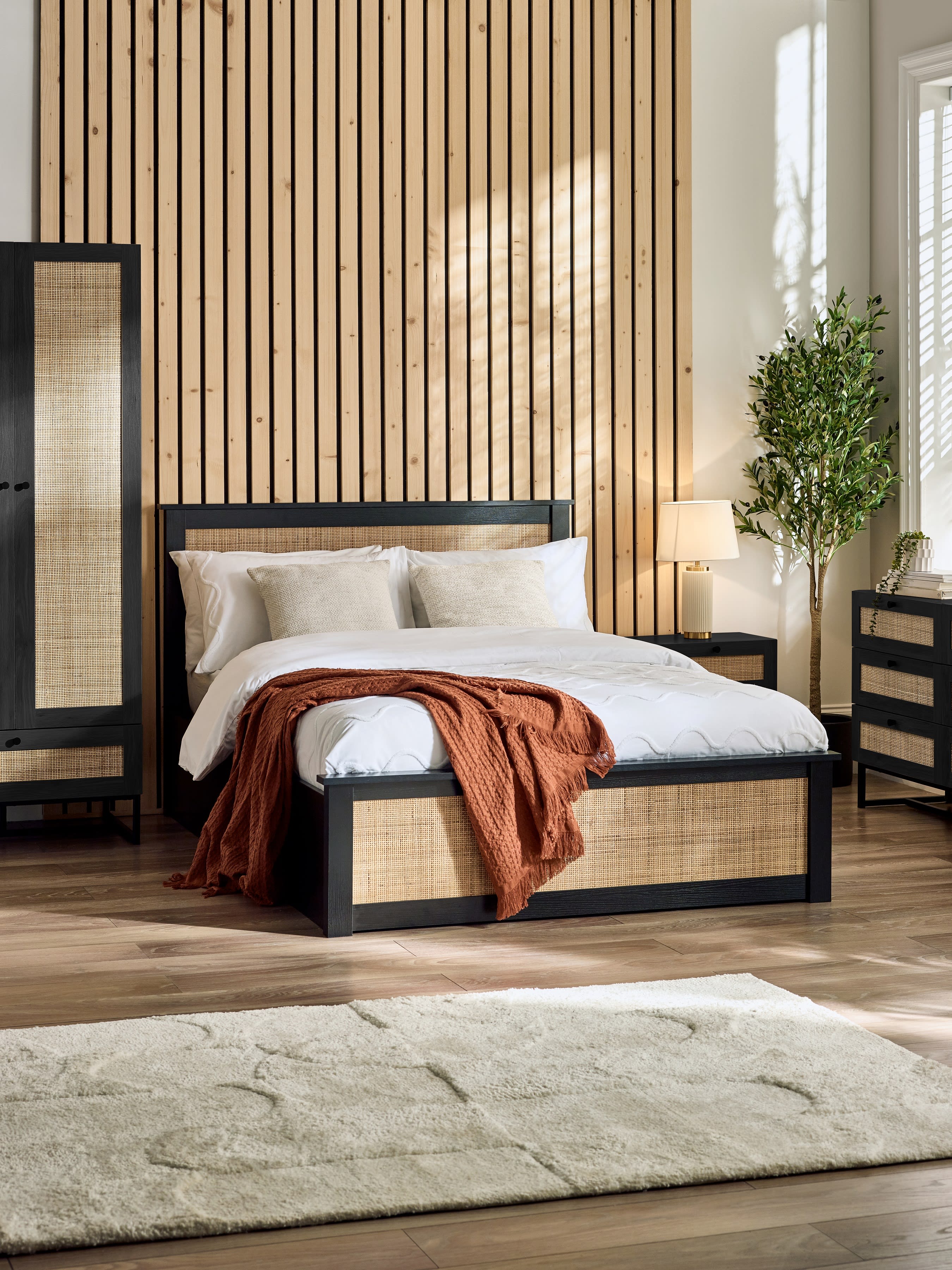 Julian Bowen Padstow ottoman bed in black with rattan panels, in a bedroom with a slatted wall