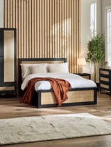 Julian Bowen Padstow ottoman bed in black with rattan panels, in a bedroom with a slatted wall