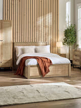 Julian Bowen Padstow ottoman bed in oak effect with rattan panels, in a bedroom with a slatted wall