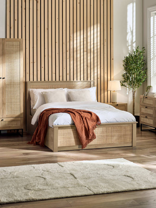 Julian Bowen Padstow ottoman bed in oak effect with rattan panels, in a bedroom with a slatted wall