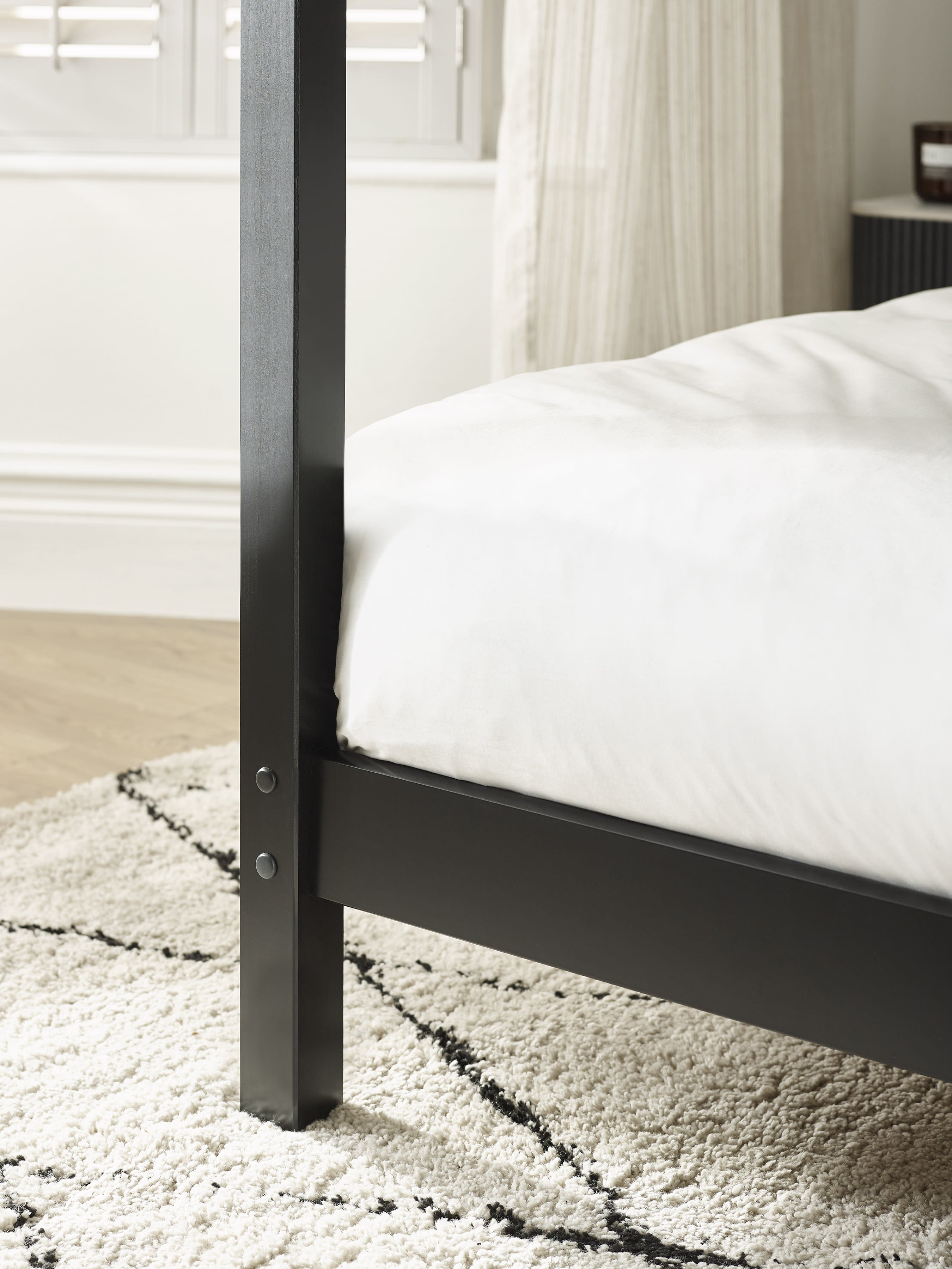 Roxanne canopy bed: black post and side rail in a bedroom, close up
