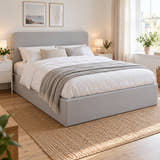 Brompton side lift ottoman bed in soft grey velvet with a rounded headboard, in a bright bedroom (AI-generated illustration of this frame; bedding for illustration, mattress not included)