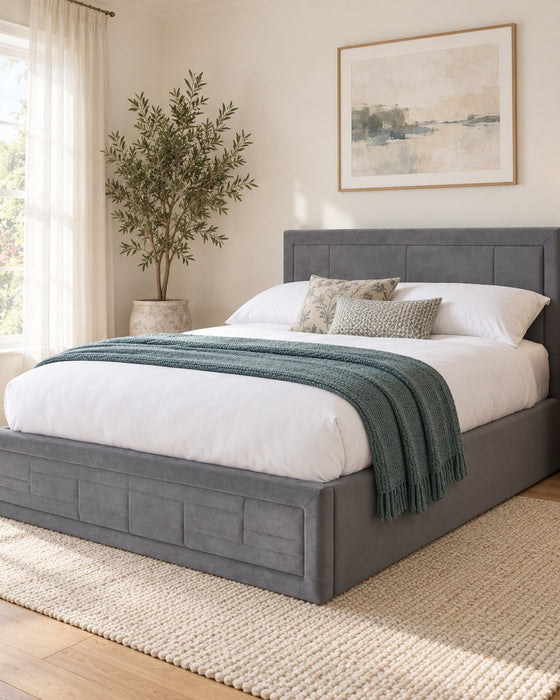 Holland grey velvet ottoman bed frame with a panelled headboard in a bright bedroom (AI-generated illustration of this frame; bedding for illustration, mattress not included)